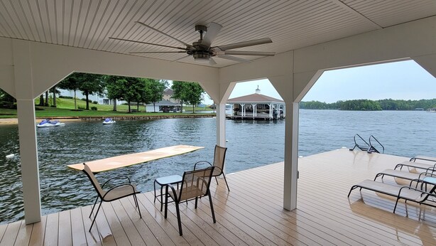 Une terrasse couverte, dotée d’une table et de chaises, qui offre une vue sur un lac où l’on aperçoit des bateaux, ainsi que sur un kiosque situé au loin.