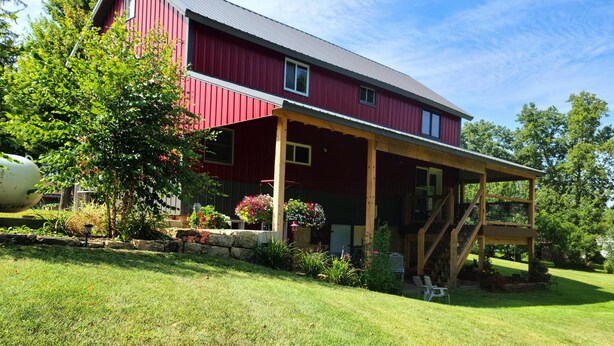 A red barn with a covered porch and a stone foundation. - The Barn House Lodge (Spillville)