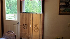 A room with a window, a door, a table, a chair, and a potted plant. - The Barn House Lodge (Spillville)