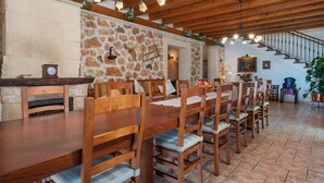 A dining area with a long wooden table and chairs, stone walls, and a staircase leading to another level. - SON LLORINGO - Beautiful villa with private above ground pool, a beautiful garden and view (Manacor)