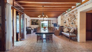 A spacious dining area with a long table and chairs, wooden ceiling beams, stone walls, and a view through the open door. - SON LLORINGO - Beautiful villa with private above ground pool, a beautiful garden and view (Manacor)