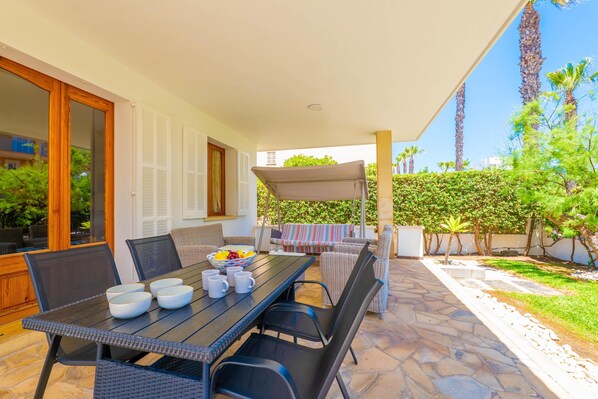 An outdoor patio with a table set for dining, surrounded by wicker chairs and a covered seating area.