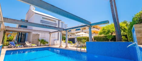 A swimming pool with lounge chairs, a covered patio area, and a modern building in the background.