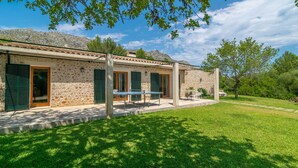Un edificio de piedra con techo de tejas, contraventanas verdes y un patio con mobiliario exterior.