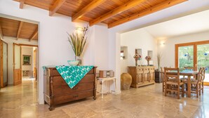 Una habitación amplia con techo de madera, zona de comedor con mesa y sillas, y un ventanal que ofrece vistas a zonas verdes.