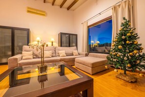 A living room with a sofa set, a glass-top coffee table, a Christmas tree, and a large window.