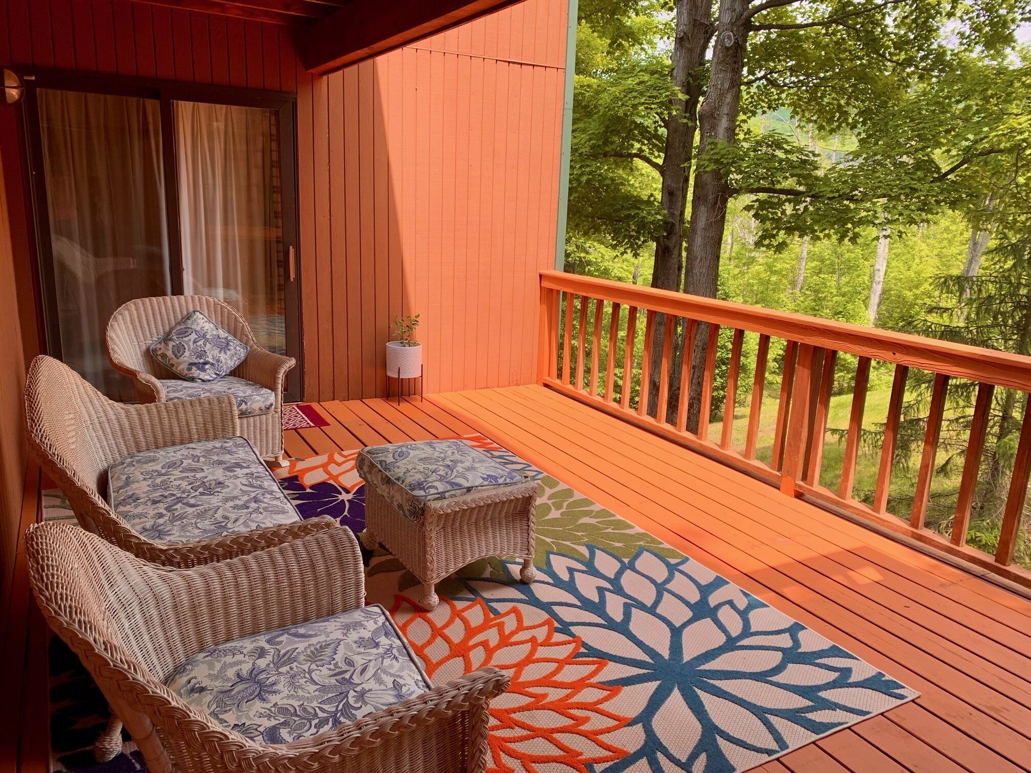 A wooden deck with wicker furniture and a colorful rug.