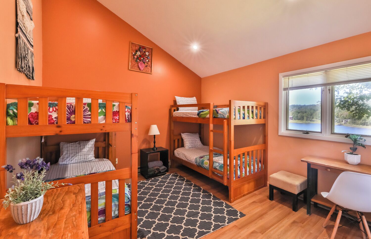 A room with two bunk beds, a desk, a chair, a lamp, and a window with a view.