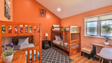 A room with two bunk beds, a desk, a chair, a lamp, and a window with a view.