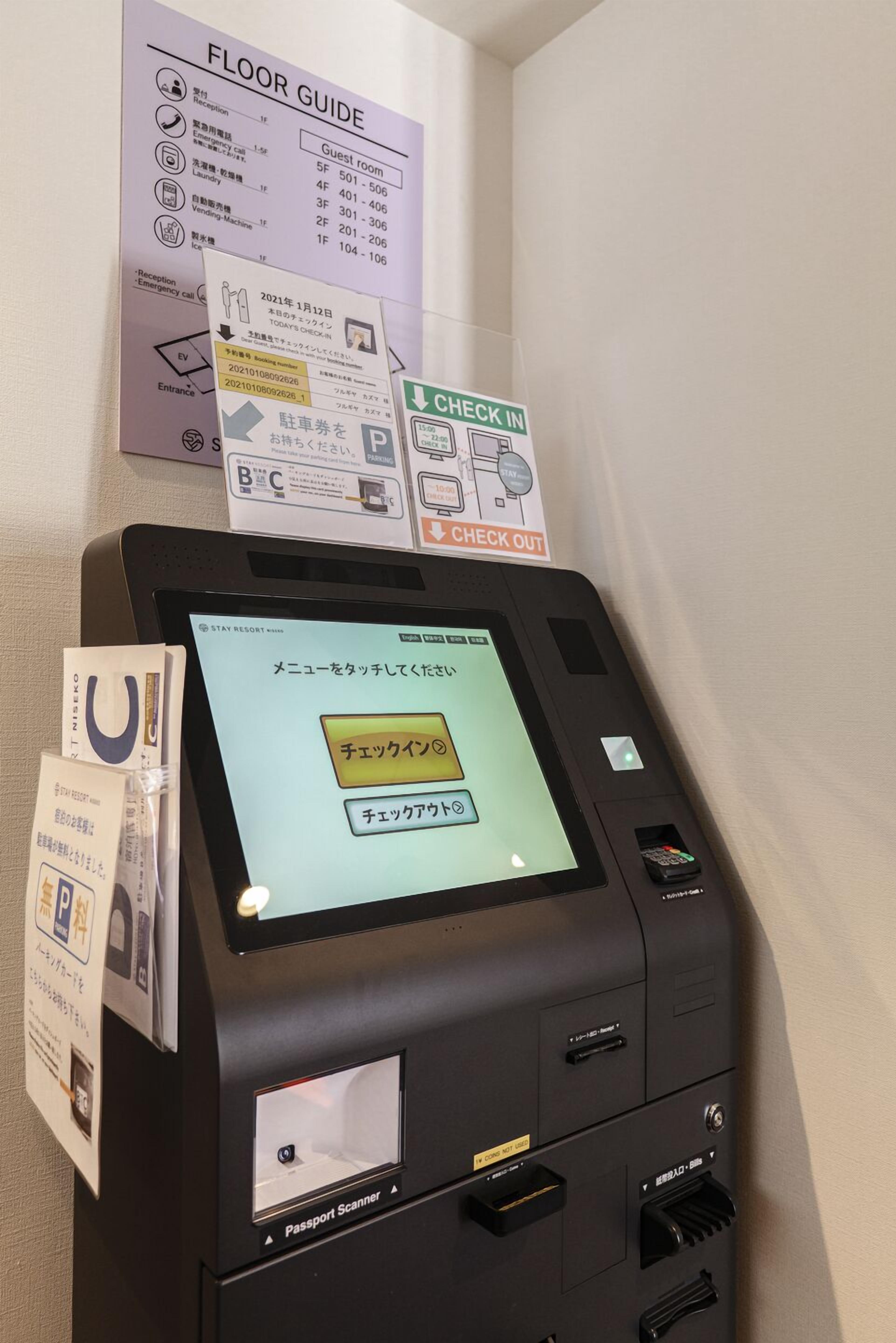 Ein Check-in-Terminal mit einem Bildschirm, der eine Meldung in Japanisch anzeigt, einem Reisepass-Scanner darunter und einem Bodenplan-Schild darüber.