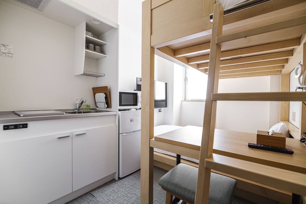 A compact hotel room with a kitchenette, a bunk bed, a desk, and a television.