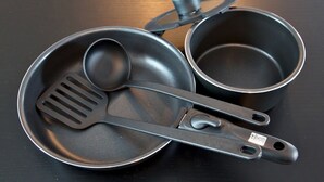 Un ensemble d’ustensiles de cuisine noirs comprenant une poêle, une casserole et une louche, posés sur une surface sombre.