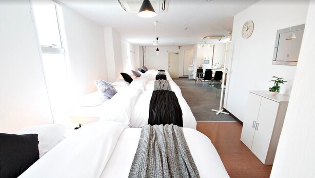 Une chambre d’hôtel avec un grand lit, un bureau, une chaise, une armoire et, au fond, une petite cuisine.