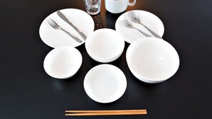 Une table dressée avec des assiettes blanches, des bols, une tasse, un verre et des baguettes.