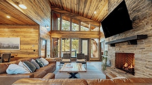 A spacious living room with a large leather sofa, a wooden coffee table, and a stone fireplace. - Panoramic Views | Sauna · Hot Tub · Game Room (Broken Bow)