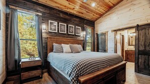 A wooden cabin bedroom with a large bed, a nightstand, a dresser, and a window with curtains. - Panoramic Views | Sauna · Hot Tub · Game Room (Broken Bow)