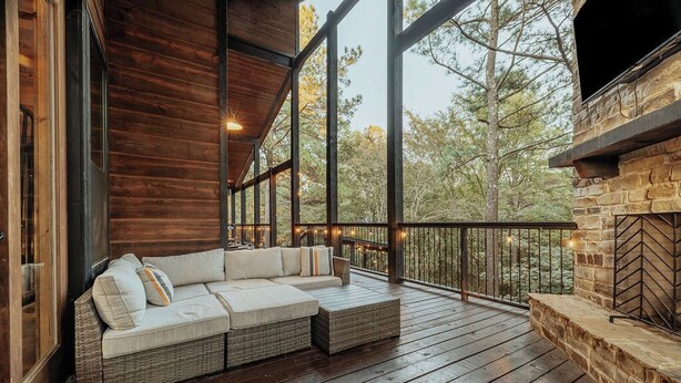 A wooden deck with a built-in sofa and stone fireplace. - Panoramic Views | Sauna · Hot Tub · Game Room (Broken Bow)