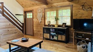 Un interior de madera con una escalera, un atrapasueños, un televisor y una estantería.