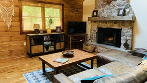 Una sala de estar acogedora con paredes de madera, una chimenea de piedra, un sofá de cuero y un televisor.