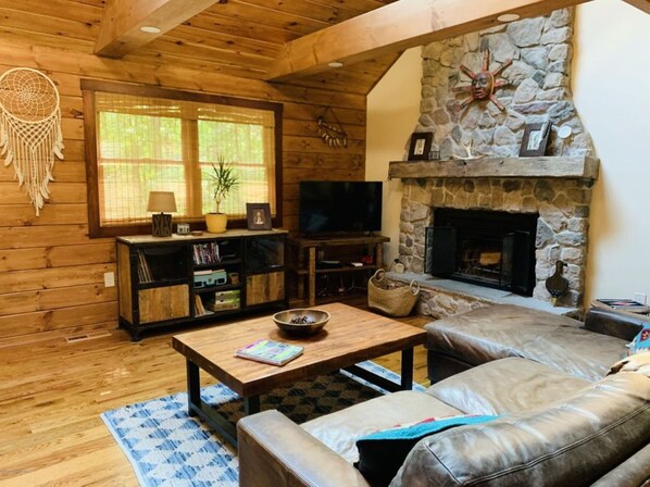 Una sala de estar acogedora con paredes de madera, una chimenea de piedra, un sofá de cuero y un televisor.