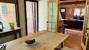 Una mesa de madera para comer con un mantel individual y un bol lleno de piñas. Hay un banco al final de la mesa.