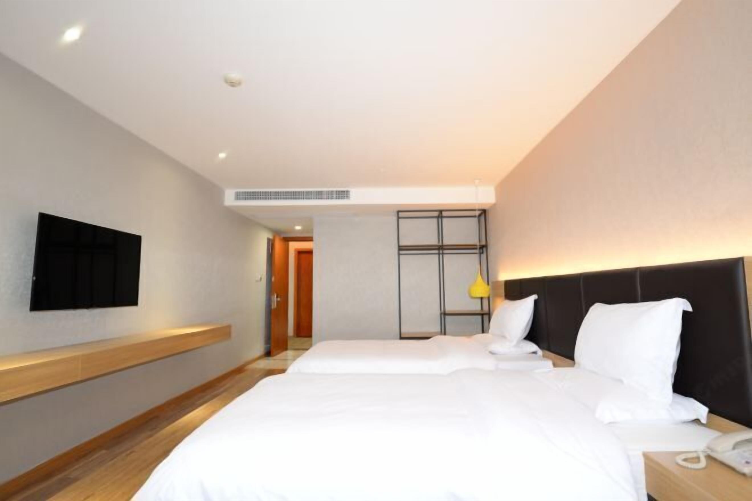 Habitación de hotel con dos camas, un televisor de pantalla plana montado en la pared, una mesita de noche con teléfono y un diseño moderno con detalles de madera.