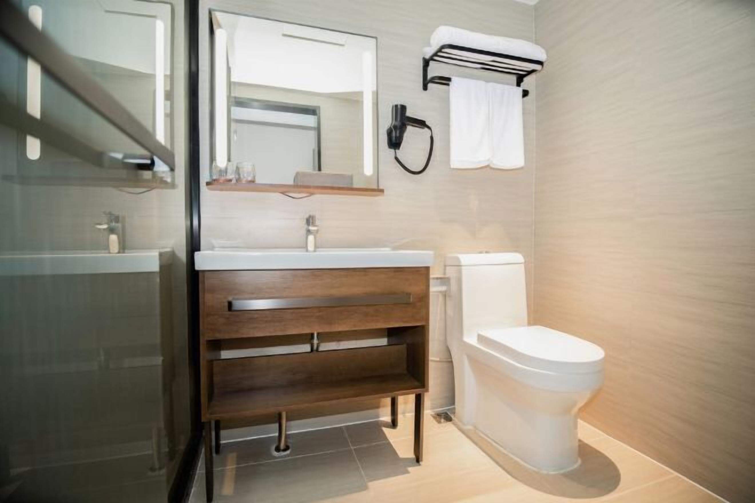 Ein modernes Badezimmer mit Duschkabine aus Glas, einem hölzernen Waschtisch mit Spiegel, Toilette und Handtuchhalter.
