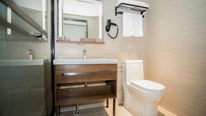 A modern bathroom with a glass shower enclosure, a wooden vanity with a mirror, a toilet, and a towel rack. - Hanting Hotel (Guangzhou Feixiang Park Metro Station) (Guangzhou)
