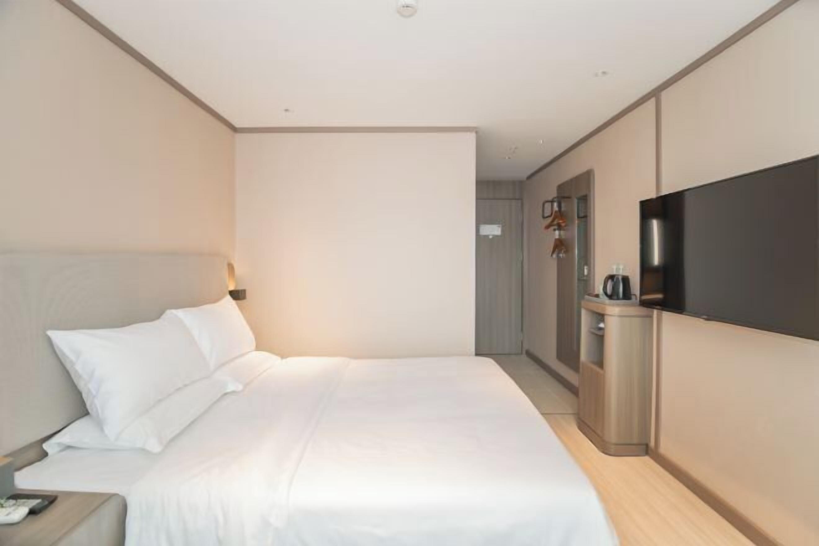 Habitación de hotel con una cama grande, un televisor montado en la pared, una mesita de noche y un armario pequeño.