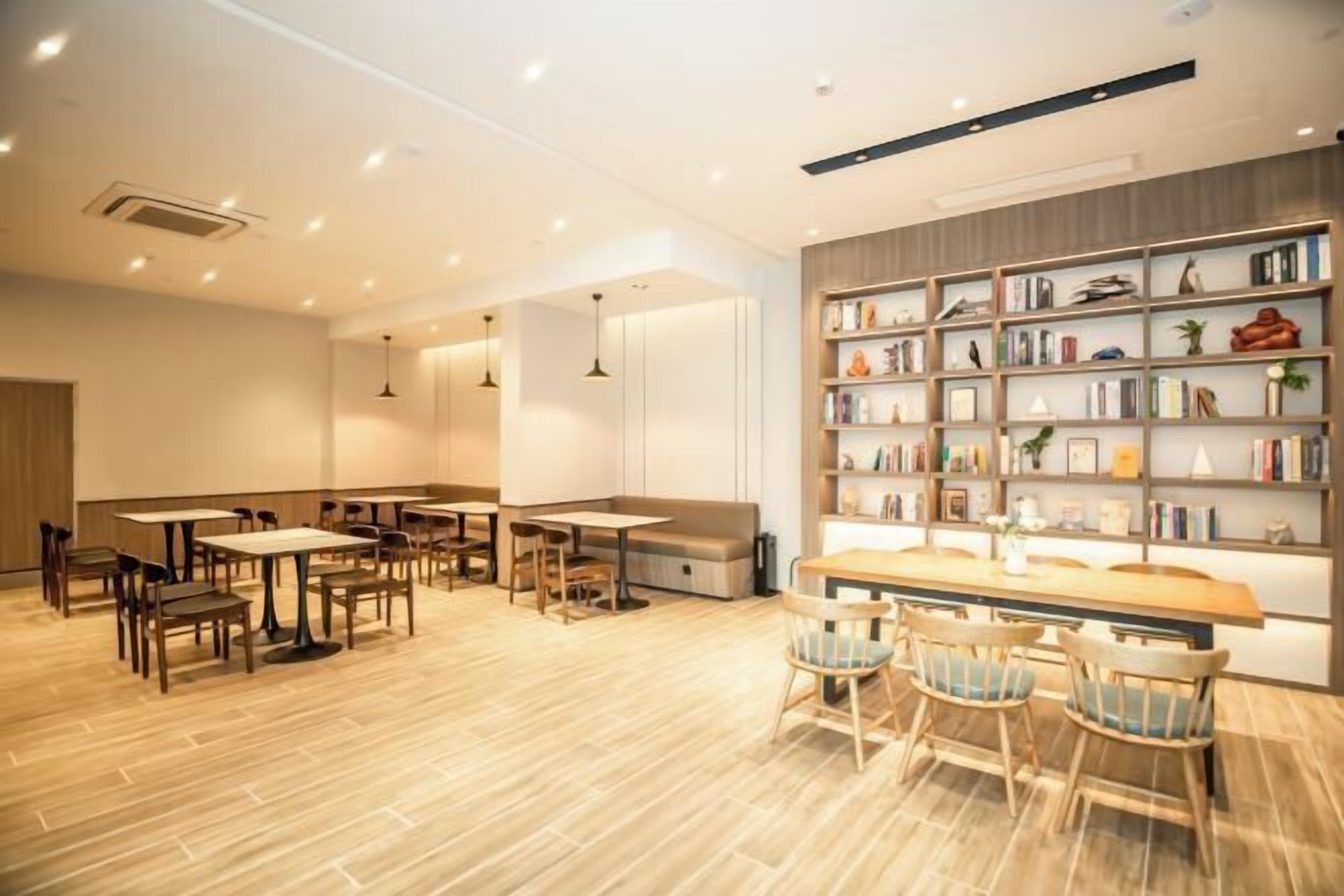 Una cafetería moderna con mesas y sillas de madera, una estantería con diversos objetos y un interior limpio y bien iluminado.