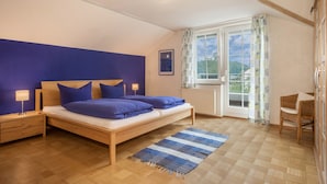 Une chambre à coucher comprenant un lit, des tables de chevet, une fenêtre avec des rideaux, une vue sur la verdure et un radiateur.