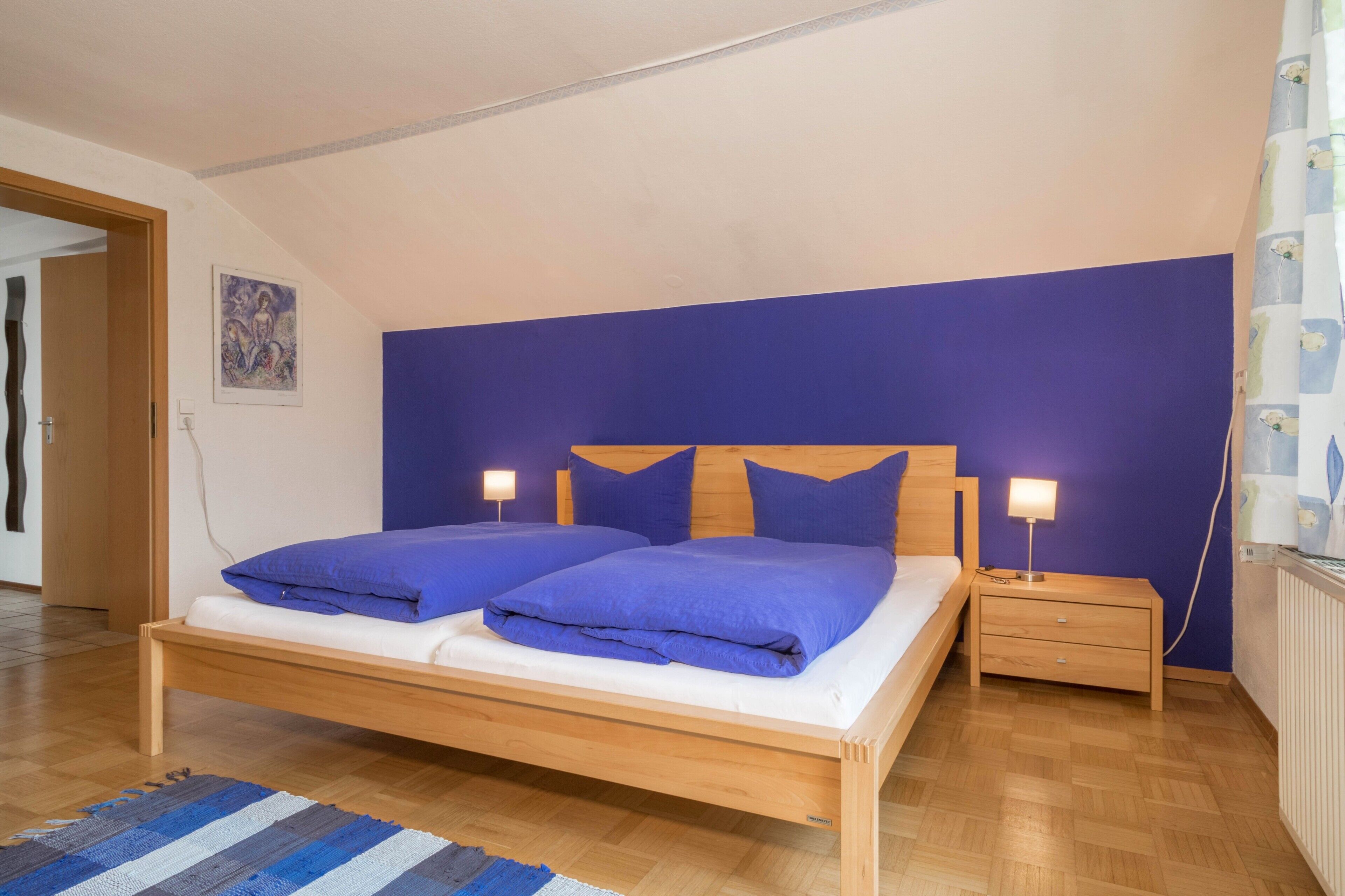 Ein Schlafzimmer mit einem hölzernen Bett, zwei Nachttischen, einer blauen Wand und einer Tür zu einem anderen Raum.