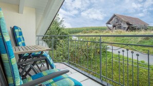 Un balcon avec une table et des chaises, une rambarde en métal et une vue sur un paysage rural avec une grange.
