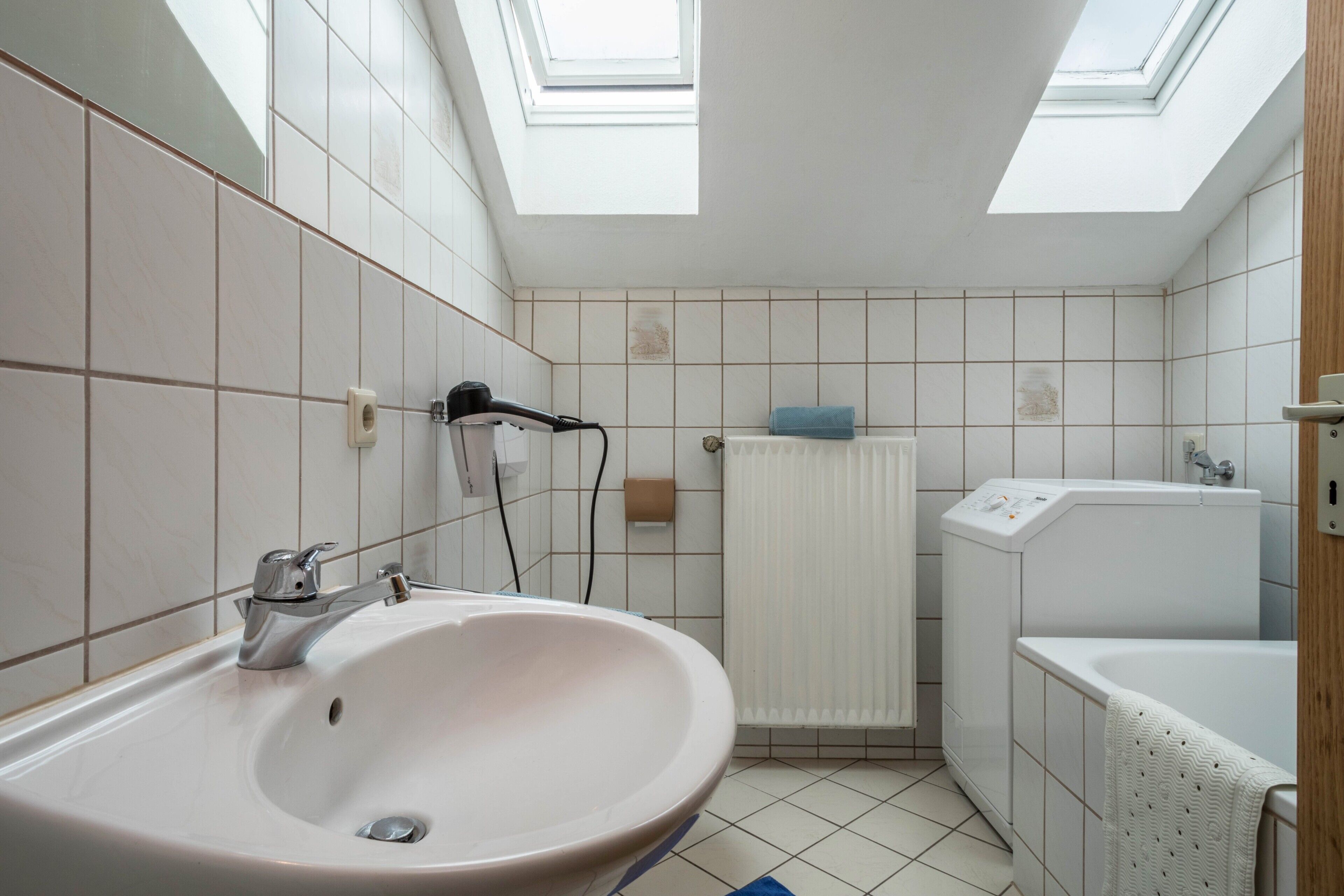 Une salle de bain équipée d’un lavabo, d’un sèche-cheveux, d’une serviette, d’une baignoire et de fenêtres de toit.