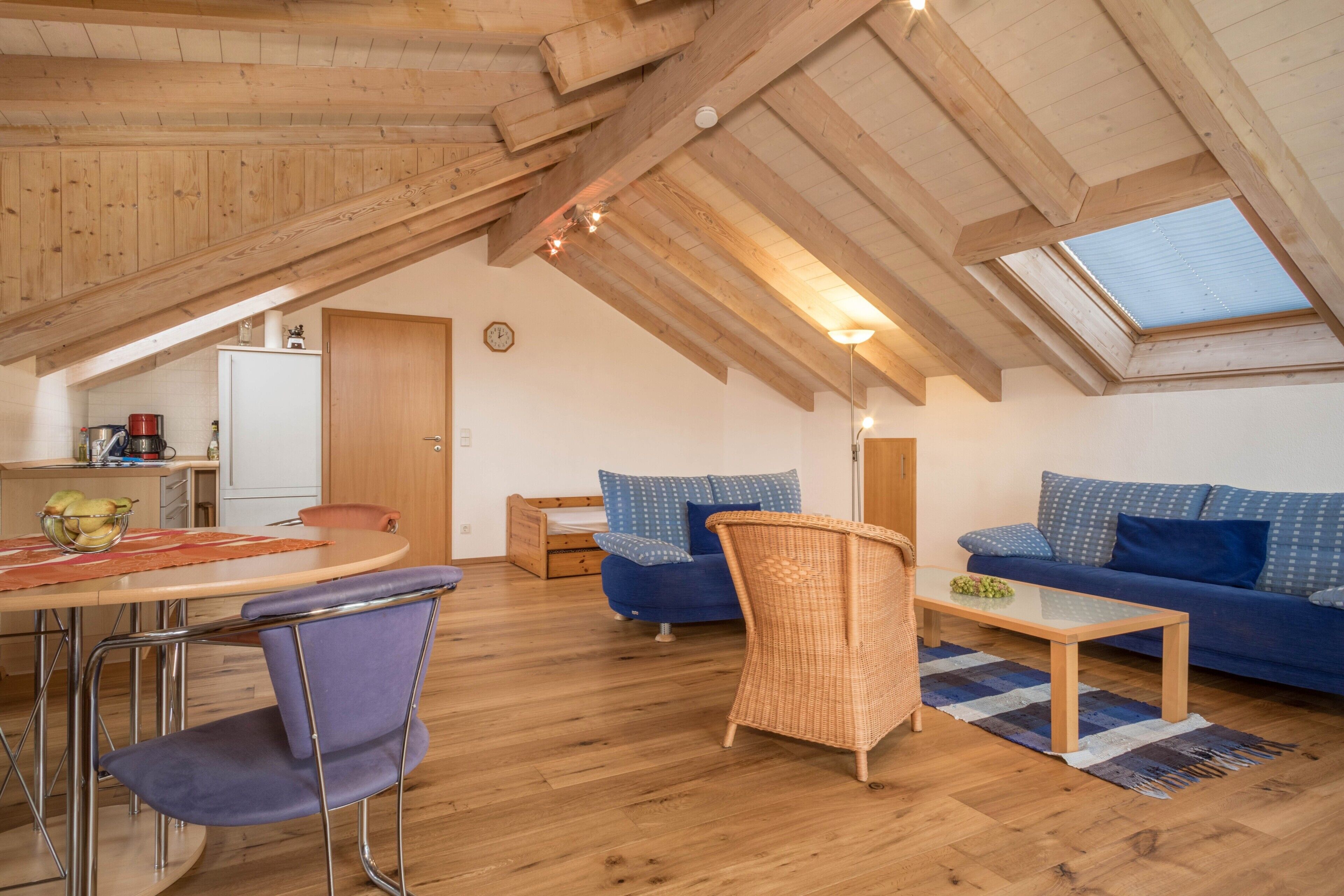 A loft-style room with a dining area, a sofa, a wicker chair, and a skylight.