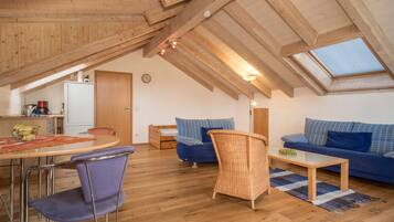A loft-style room with a dining area, a sofa, a wicker chair, and a skylight.