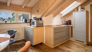 Une cuisine avec des poutres en bois, une fenêtre, un évier, un four à micro-ondes, un réfrigérateur et un coin repas avec des chaises.