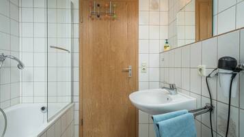 Un bany amb una porta de fusta, un lavabo blanc, una banyera i un penjador de tovalloles.