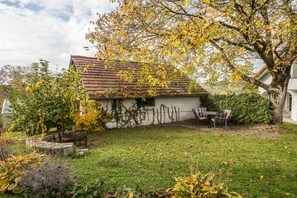 A house with a sloped roof, a small garden with a lawn, and a patio with chairs.