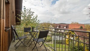 Eine Holzdielen-Terrasse mit zwei Stühlen und einem Tisch, mit Blick auf ein Wohngebiet mit Häusern und Bäumen.