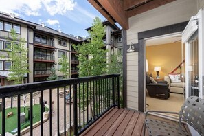A balcony with a view of neighboring buildings, a small outdoor seating area, and a glimpse of an interior living space.