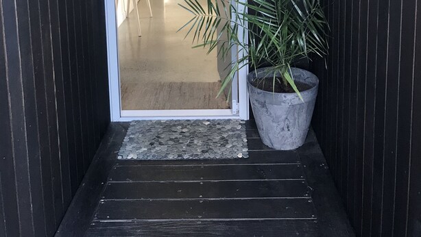 A modern entrance with a dark wooden door, a potted plant, and a clear view into a bright interior space. - Luxury Home with pool/spa; close to beach/ 4 bedroom/ 2 bath. On golf course. (Whangamata)