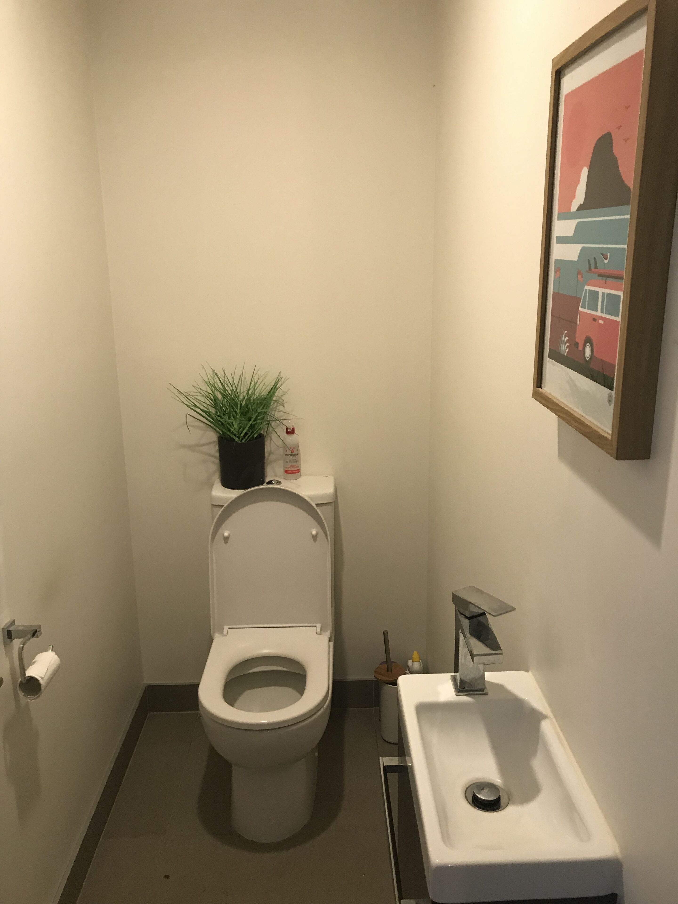 A small, modern bathroom with a toilet, sink, and a framed picture on the wall.