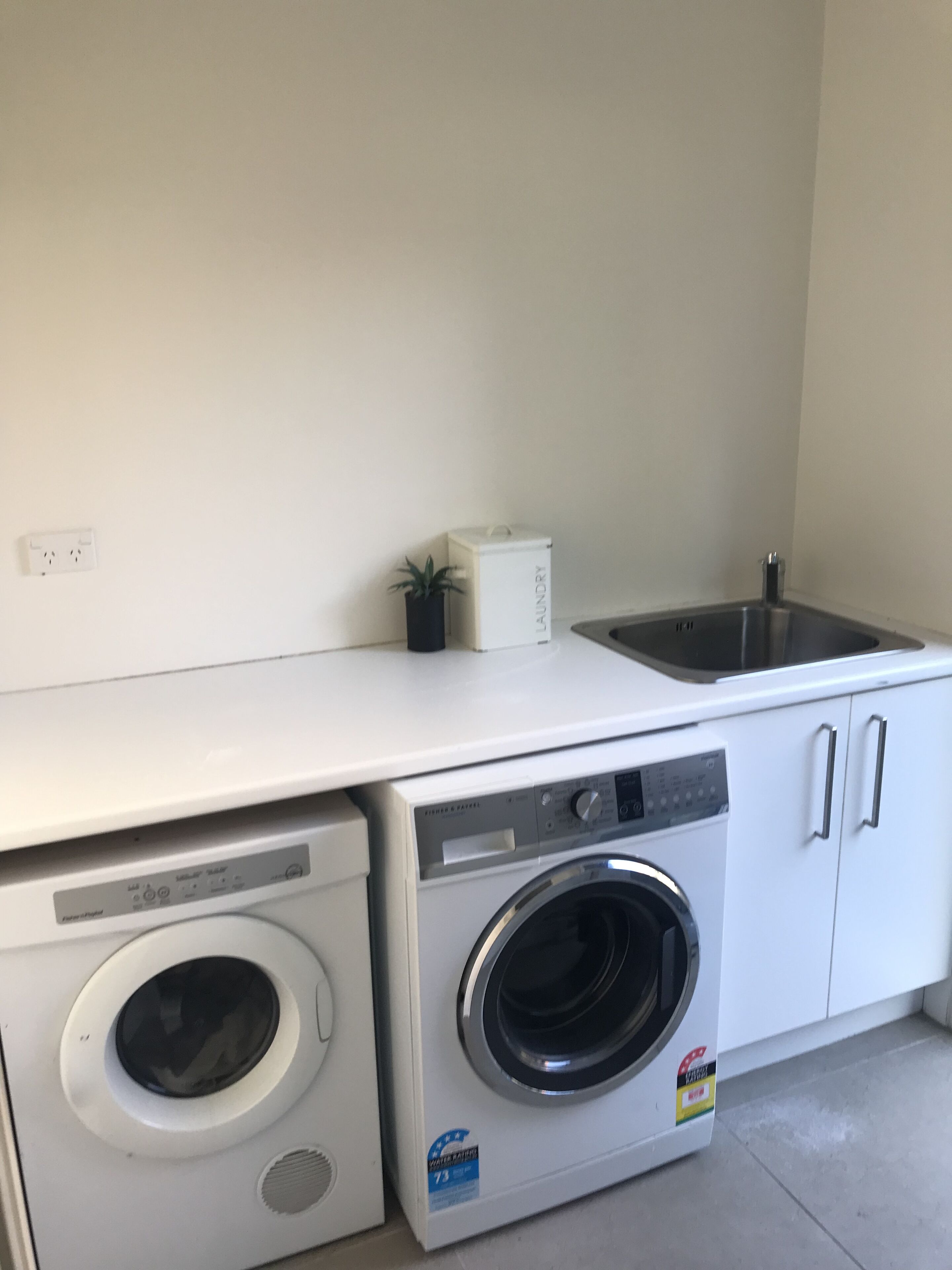 A compact laundry area with a washing machine and dryer, a small sink, and a potted plant.