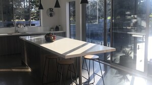 A modern kitchen with a large island, pendant lights, and a view of the outdoors. - Luxury Home with pool/spa; close to beach/ 4 bedroom/ 2 bath. On golf course. (Whangamata)