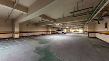 Een meerlaags parkeergarage met betonnen vloeren en wanden, met verschillende geparkeerde auto's en zichtbare constructie-elementen zoals balken en leidingen.