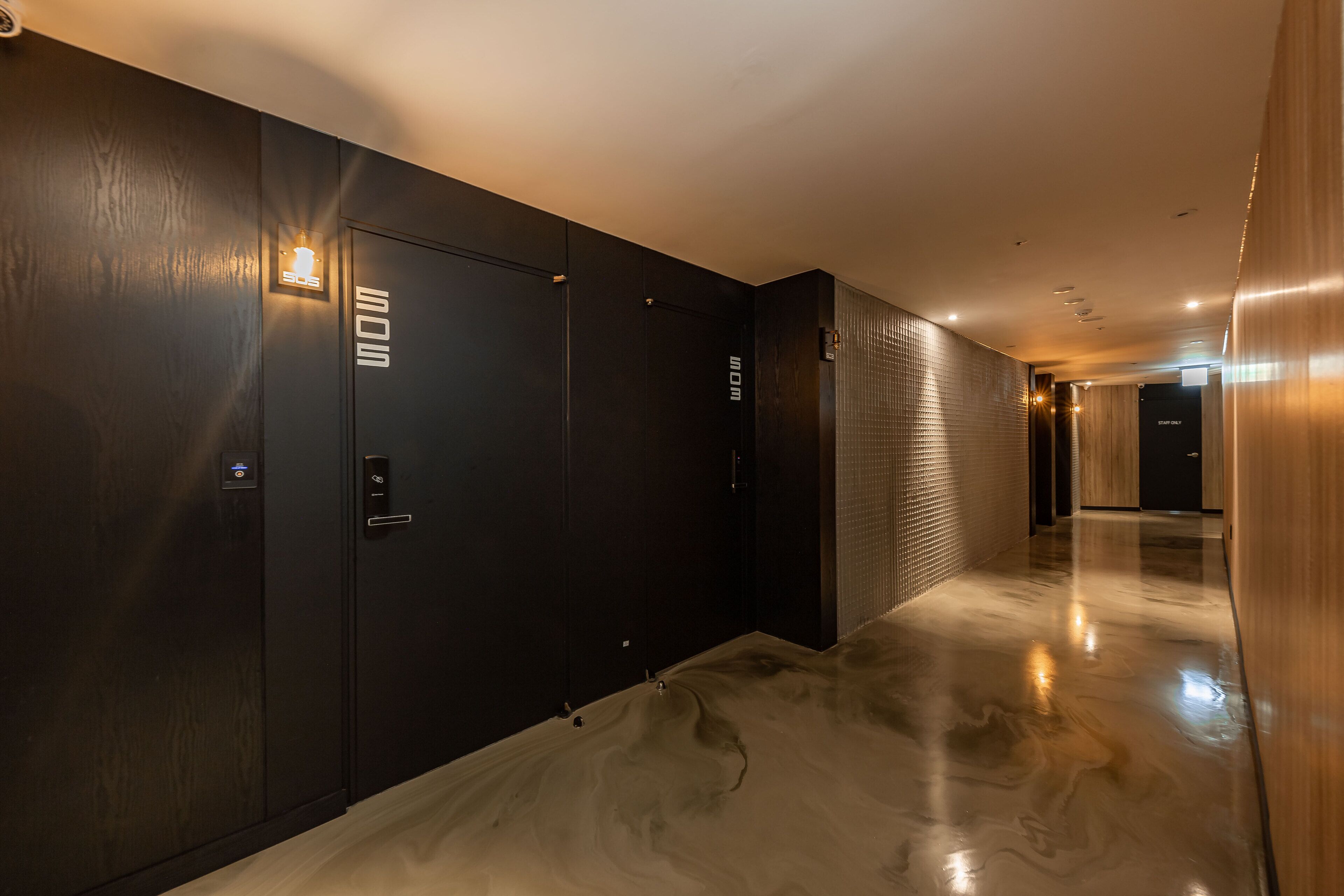 Un pasillo moderno con piso pulido, puertas de madera oscura y un accesorio de iluminación.