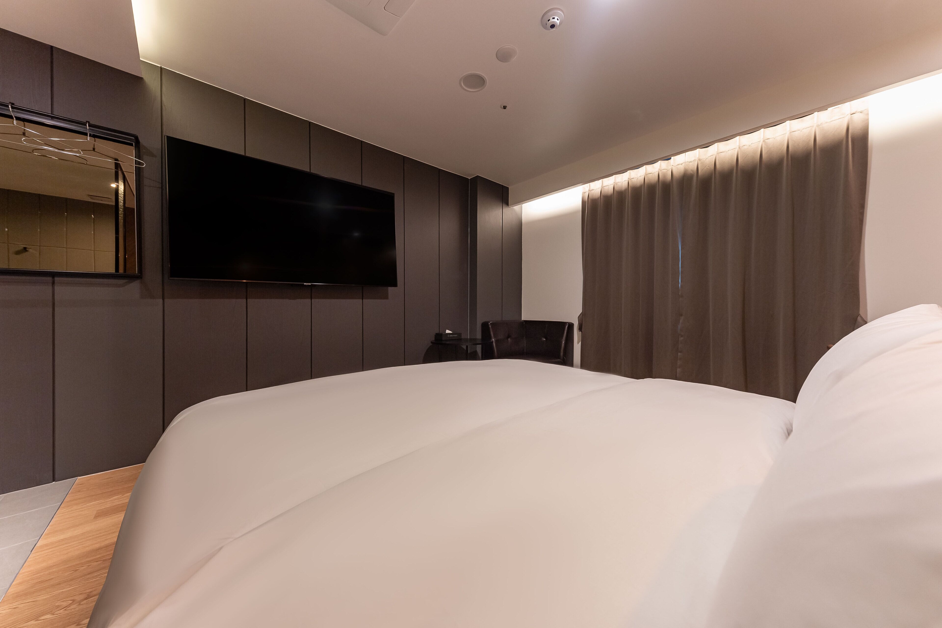 A modern hotel room with a large bed, a flat-screen TV mounted on the wall, and a large window with curtains.