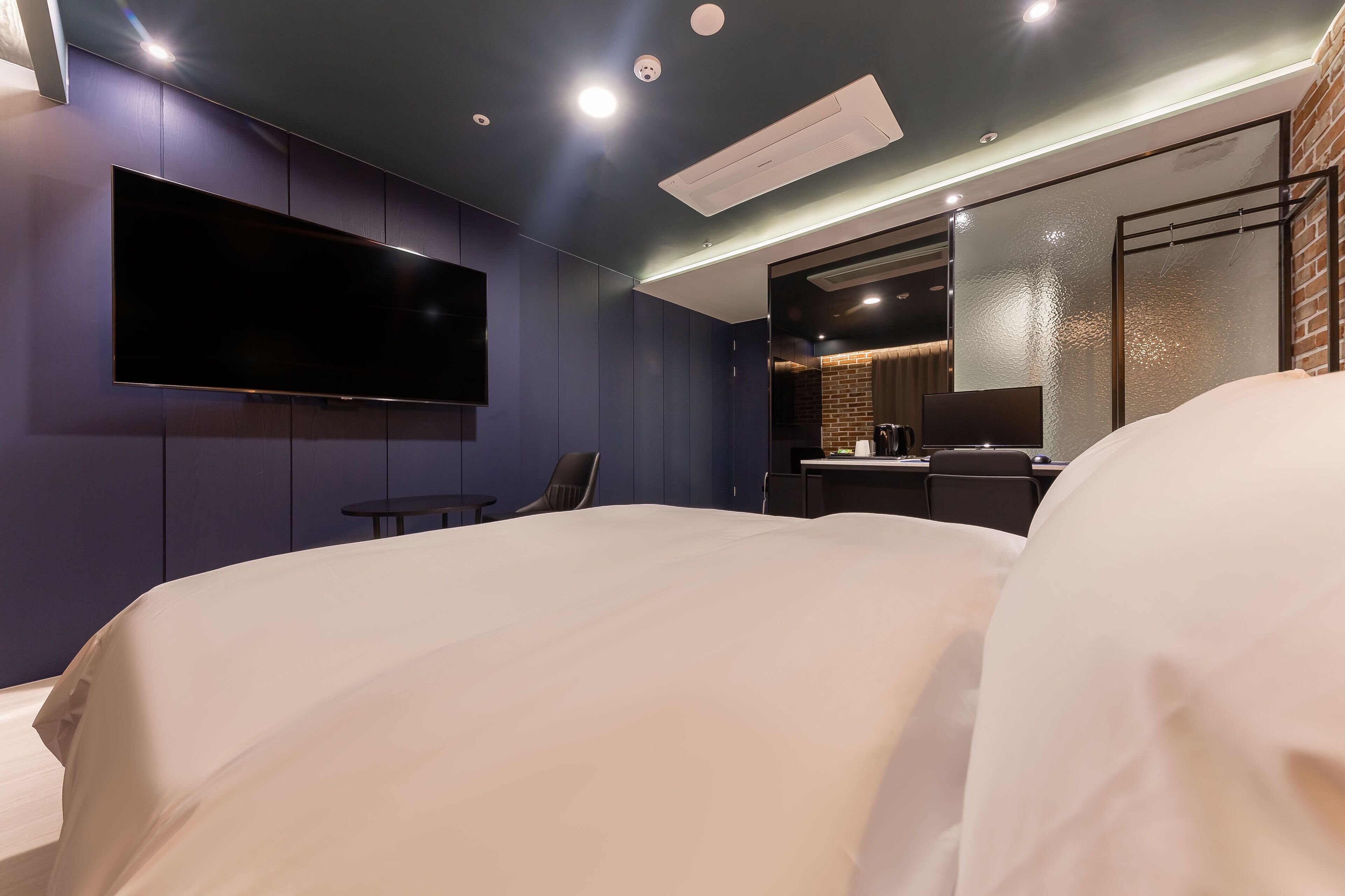 Una habitación de hotel moderna con una cama grande, un televisor de pantalla plana montado en la pared, una mesita y una zona de estar con sillones.