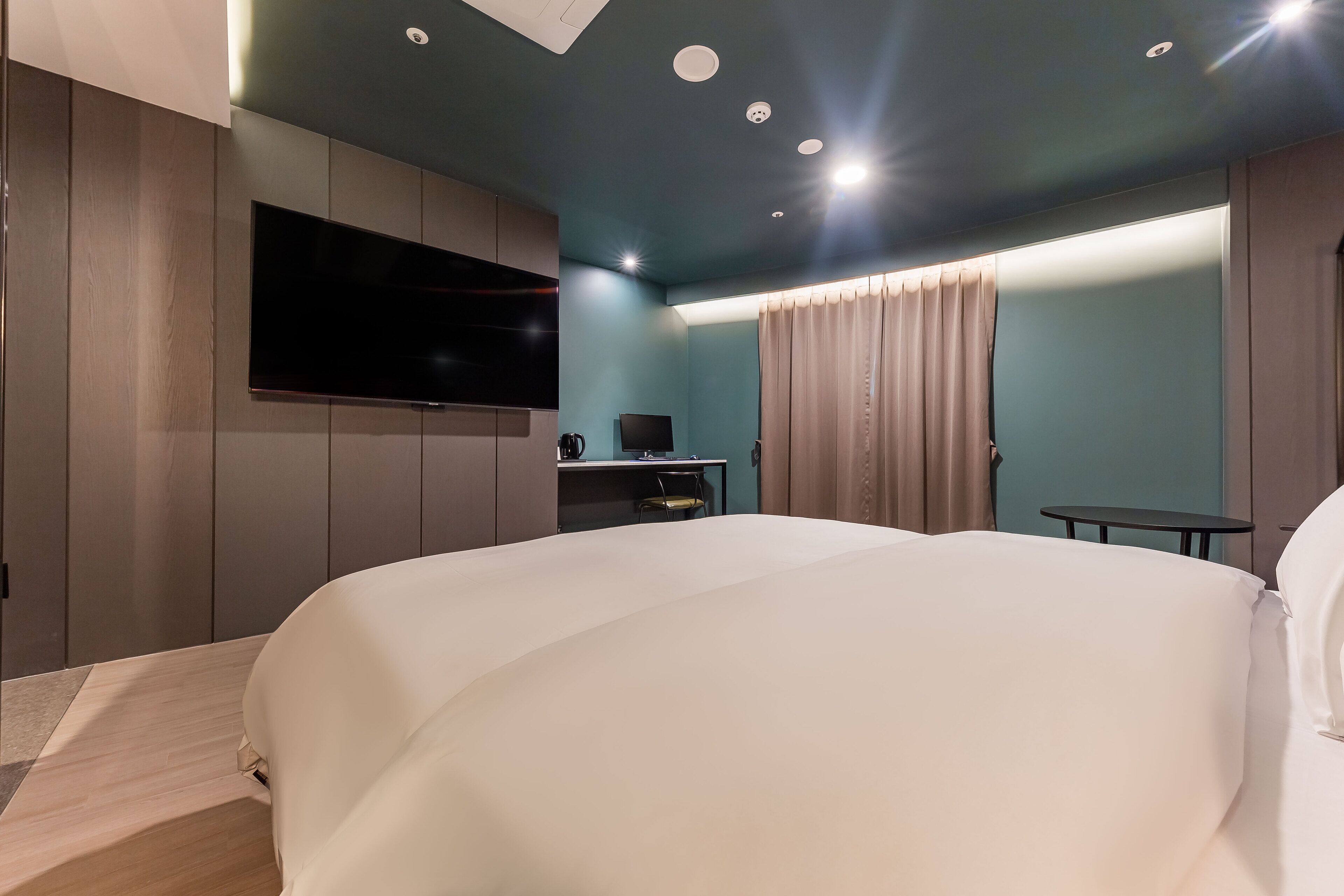 Una habitación de hotel moderna con una cama grande, un televisor de pantalla plana montado en la pared, un escritorio con una silla y una mesita.